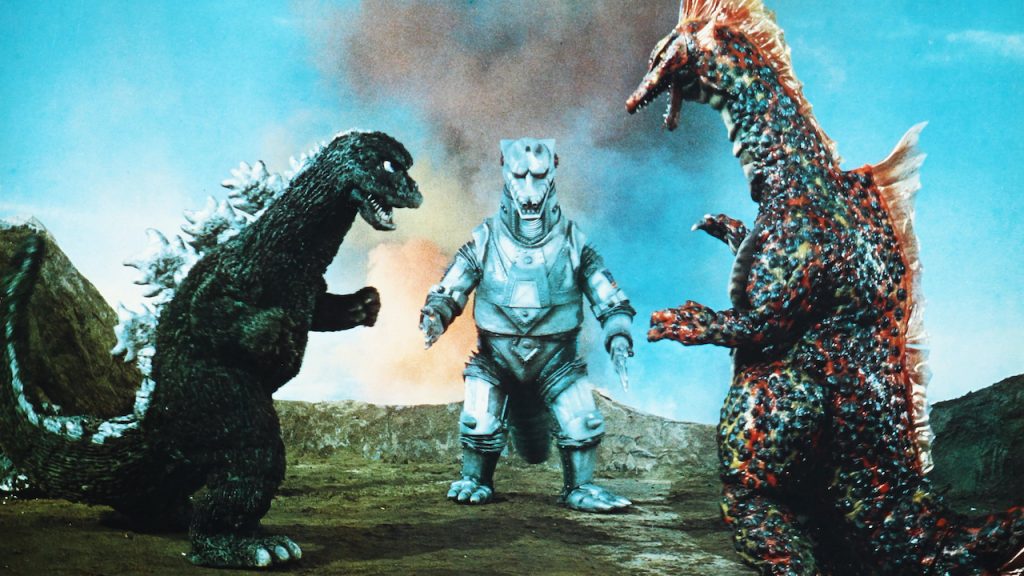 This is a film still from TERROR OF MECHAGODZILLA (メカゴジラの逆襲, Mekagojira no Gyakushū) dir by Ishirō Honda (1975) showing three giant monsters about to start fighting, two dinosaurs and a robo-dinosaur.