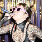 This is a picture of someone dressed in party gear and sunglasses blowing a noise maker at a screening of THE ROCKY HORROR PICTURE SHOW in Bar Paragon at Genesis Cinema.