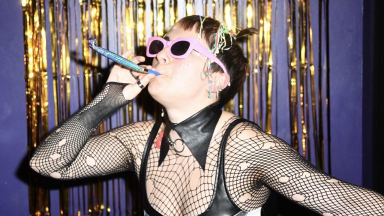 This is a picture of someone dressed in party gear and sunglasses blowing a noise maker at a screening of THE ROCKY HORROR PICTURE SHOW in Bar Paragon at Genesis Cinema.