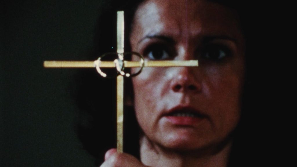 This is a film clip from SATAN WAR (1979) showing a terrified woman holding a crucifix in front of her face in a dark room. We can't see what she is afraid of...