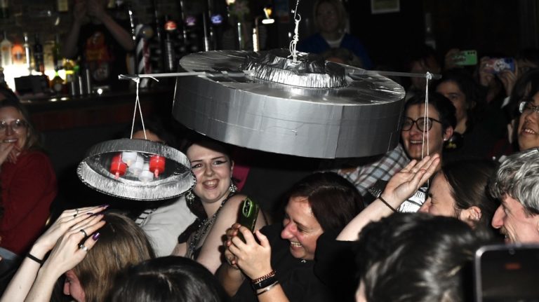 This is a photograph of our audience sat in a bar watching PLAN 9 FROM OUTER SPACE. A prop flying saucer is floating through the bar, and they are reacgting in 'terror'.
